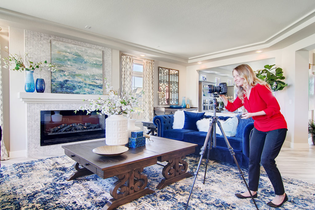 real estate photographer in living room with tripod wearing a red shirt.